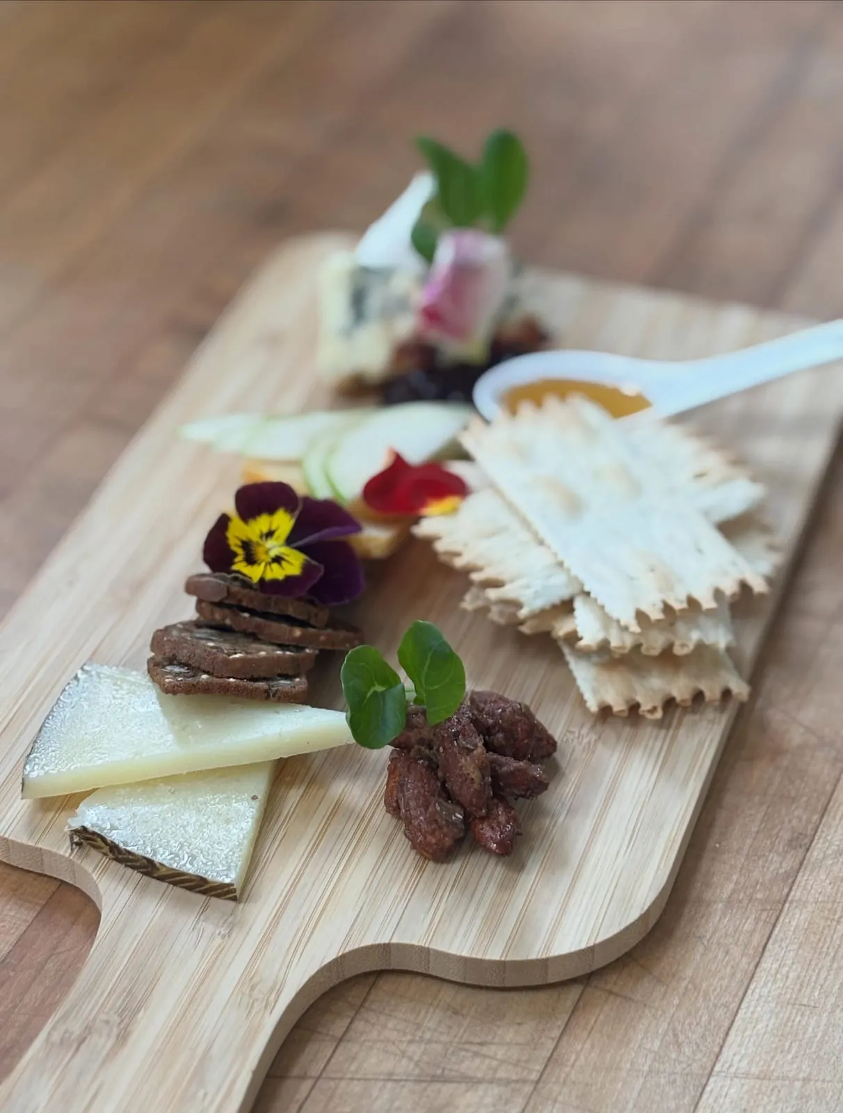 Cheese & charcuterie board with crackers, candied nuts, honey, and edible flowers